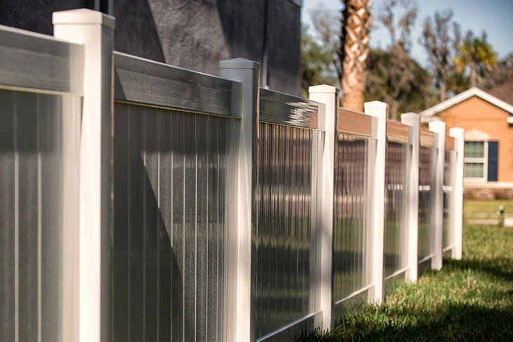 Clôture résidentielle blanche en PVC ou vinyl avec poteaux carrés et panneaux verticaux installée le long d'un chemin pavé