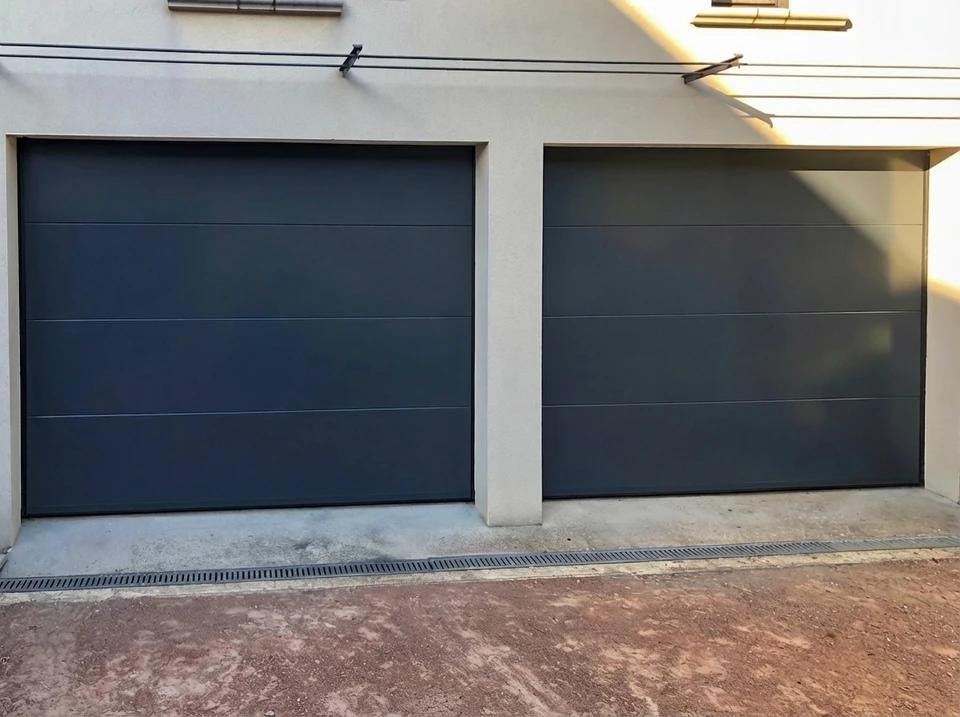 Porte de garage sectionnelle latérale à vantaux coulissants, finition lisse, coloris gris anthracite RAL 7016, installée en applique dans une baie maçonnée