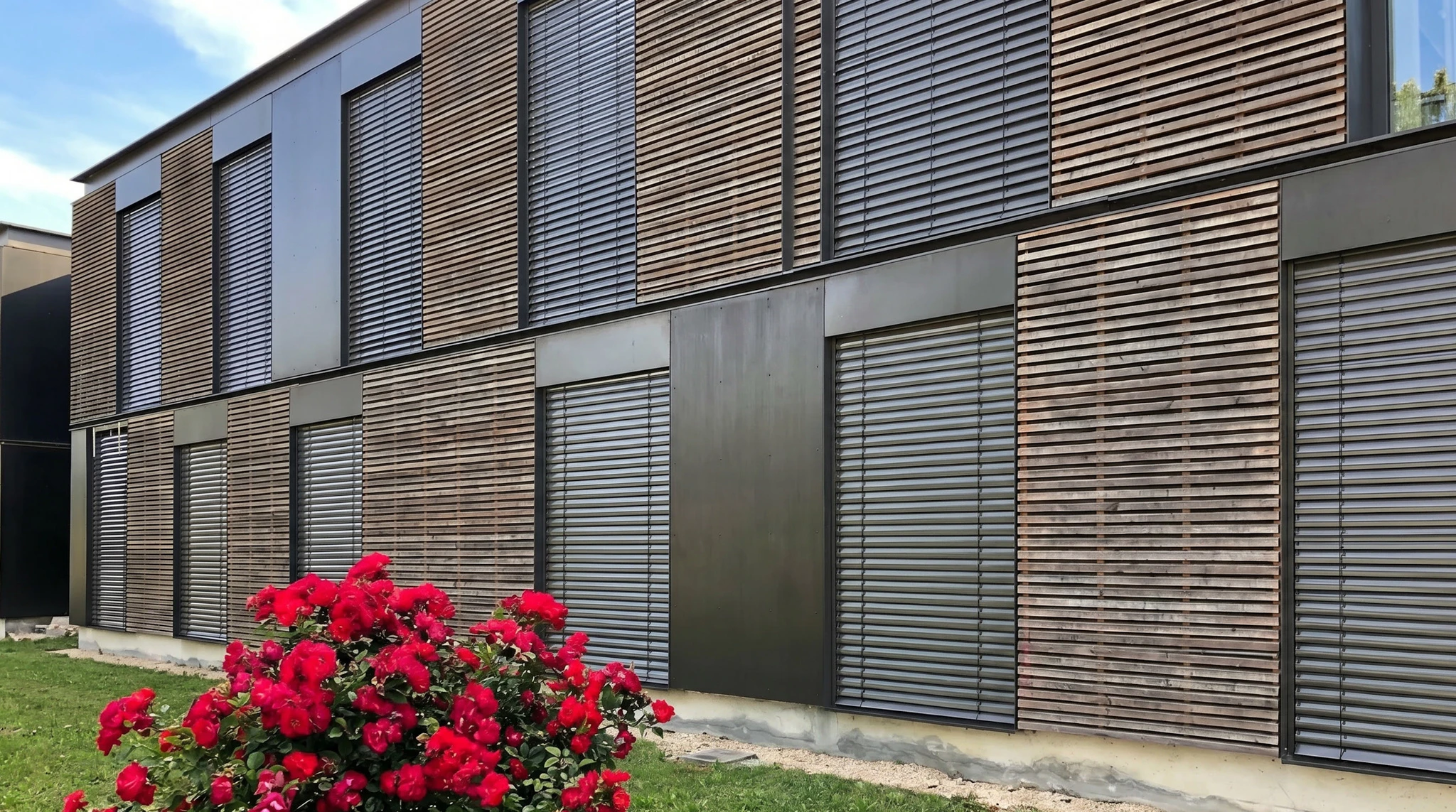 Façade extérieure d'une maison en briques rouges avec trois volets roulants blancs fermés, sous un ciel bleu dégagé