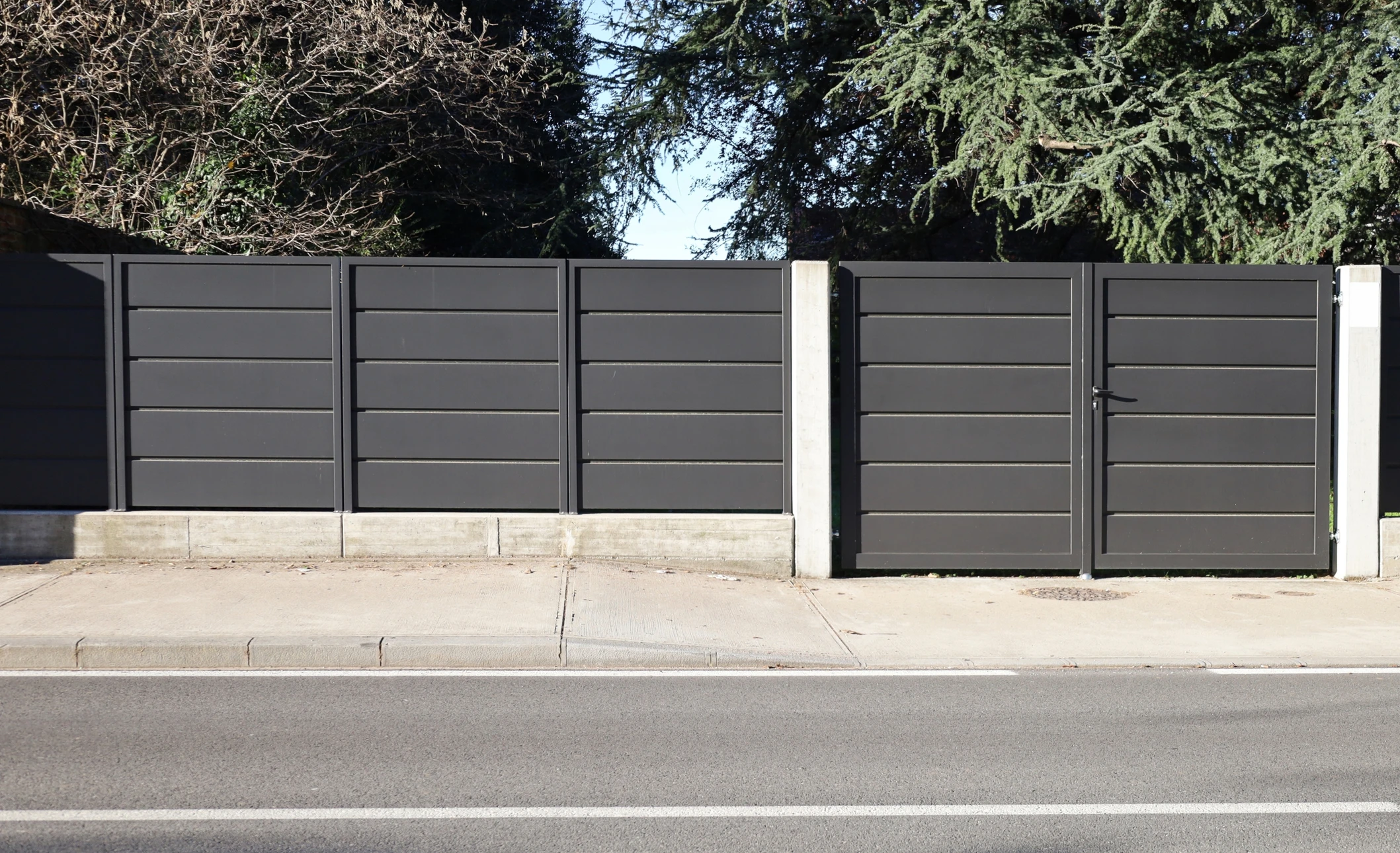Portail résidentiel en fer forgé noir avec ornements décoratifs, piliers en briques beiges, clôture assortie